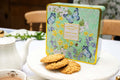 Decorative cookie tin with floral and butterfly design on a table with cookies and tea.