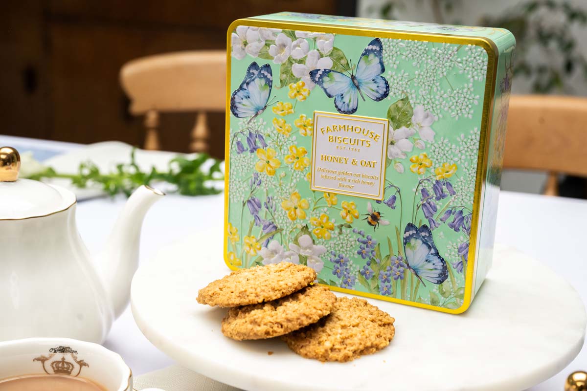 Decorative cookie tin with floral and butterfly design on a table with cookies and tea.