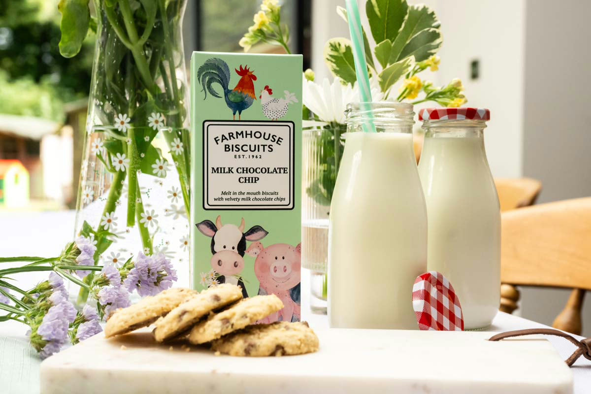 Box of Farmhouse Biscuits, cookies, and milk bottles on a table with flowers.